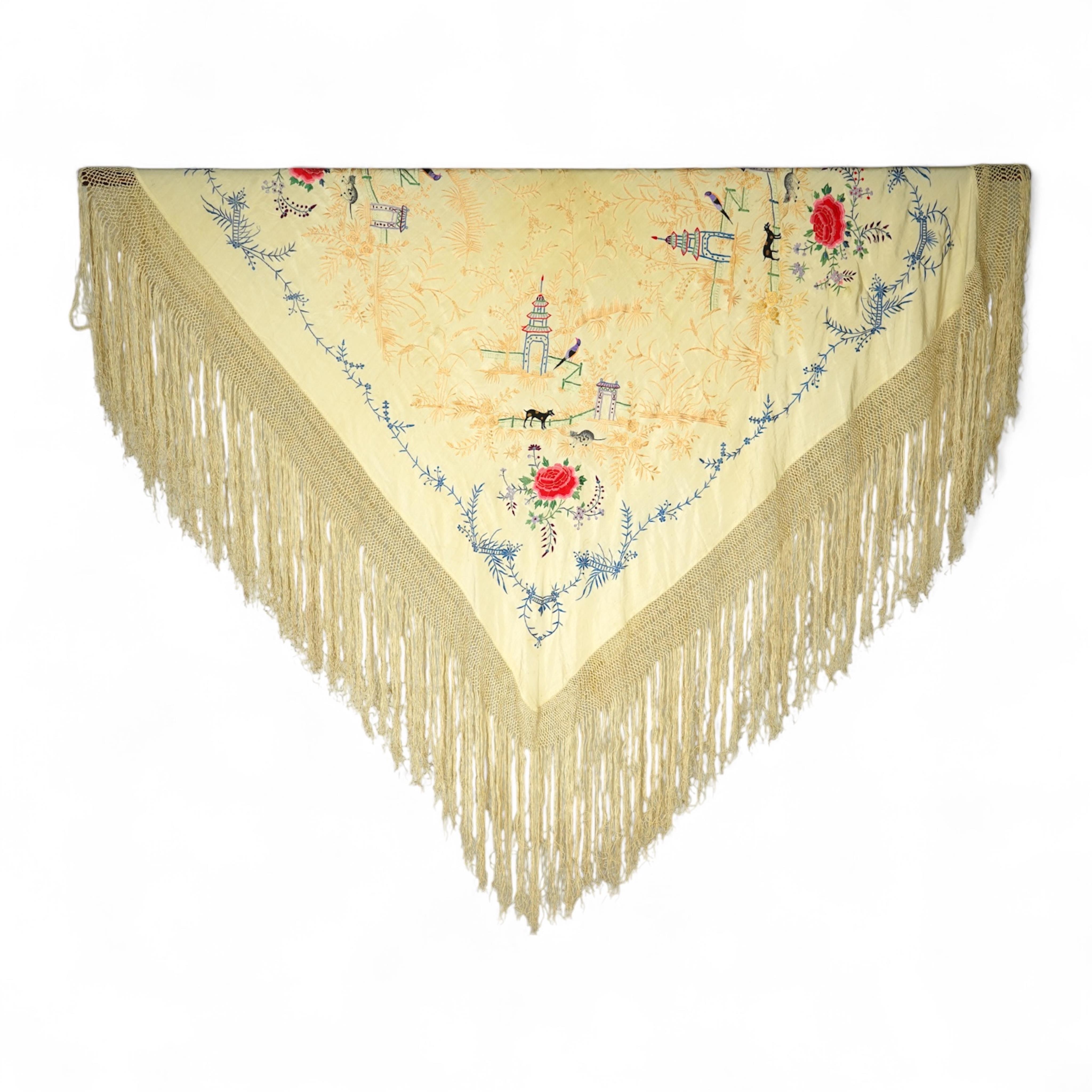 A Chinese cream silk polychrome embroidered shawl with a long fringe. Embroidered with four unusual corner cartouches of Pagoda, flowers, birds, cats and dogs. 132cm x 126cm.